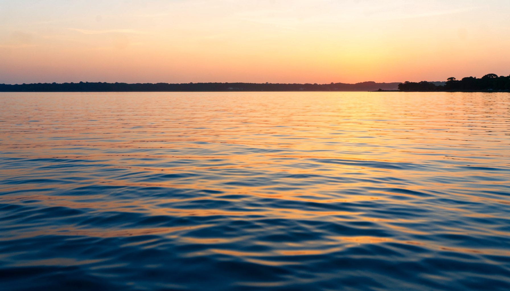 Calm water reflecting a golden sunset, warm amber tones across gentle ripples