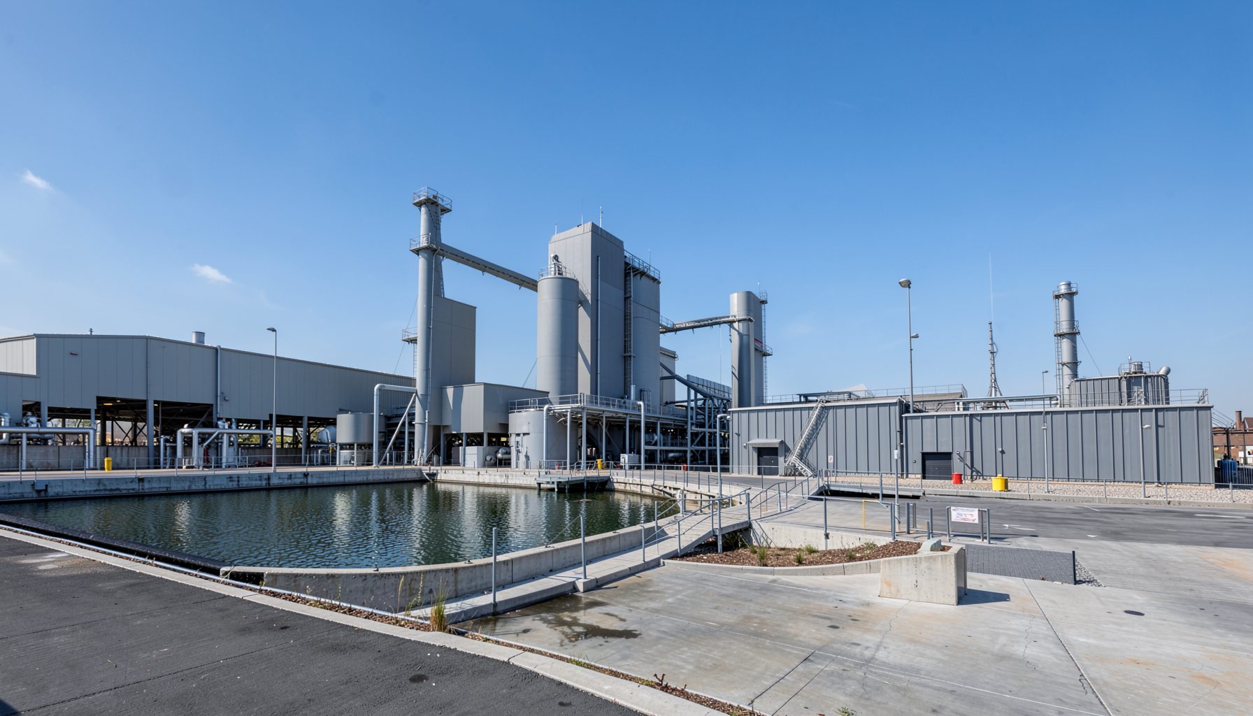 Wide view of a modern water treatment facility with blue sky and industrial structures in muted gray and steel tones